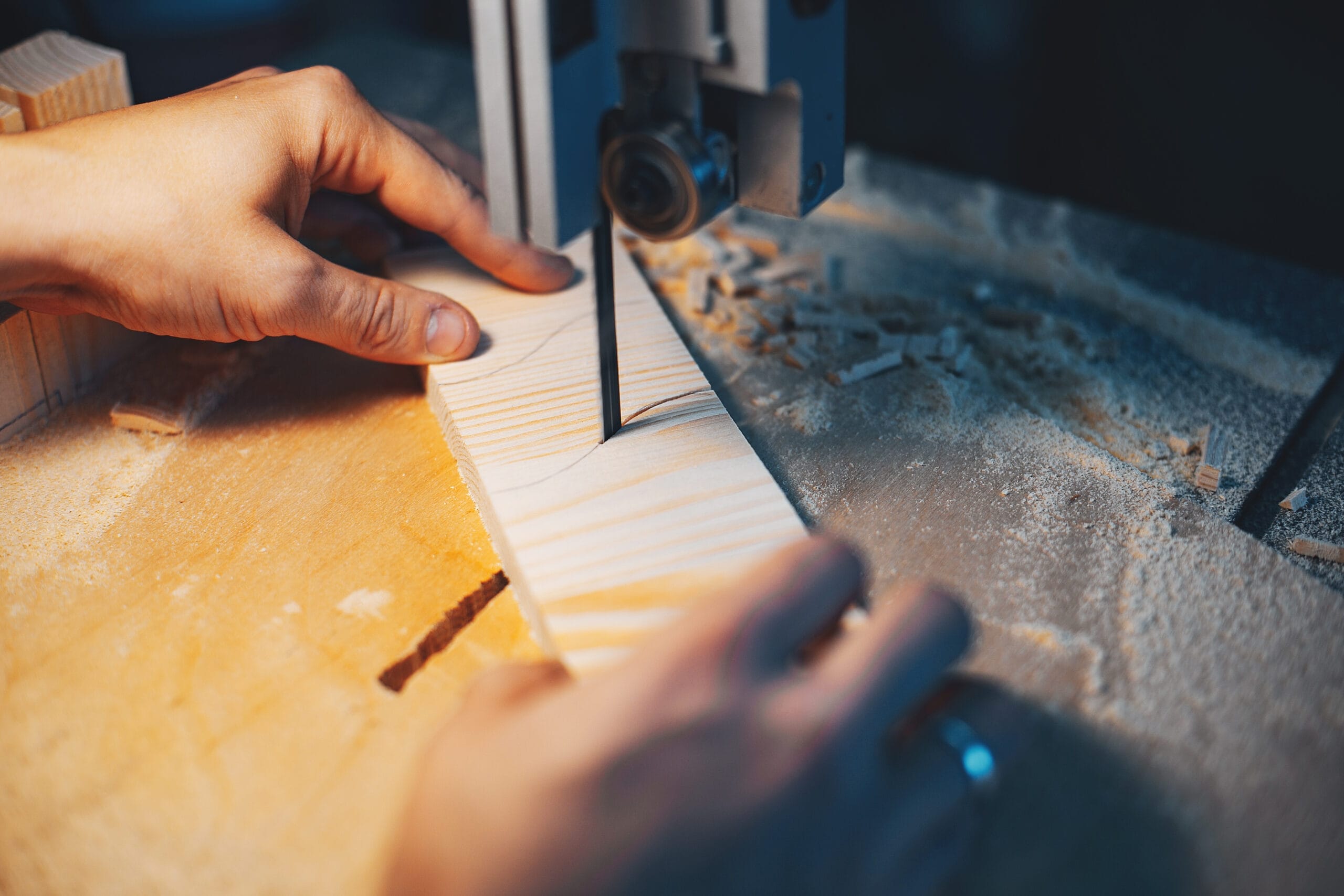 Close-up of hands using a band saw to cut a piece of wood.